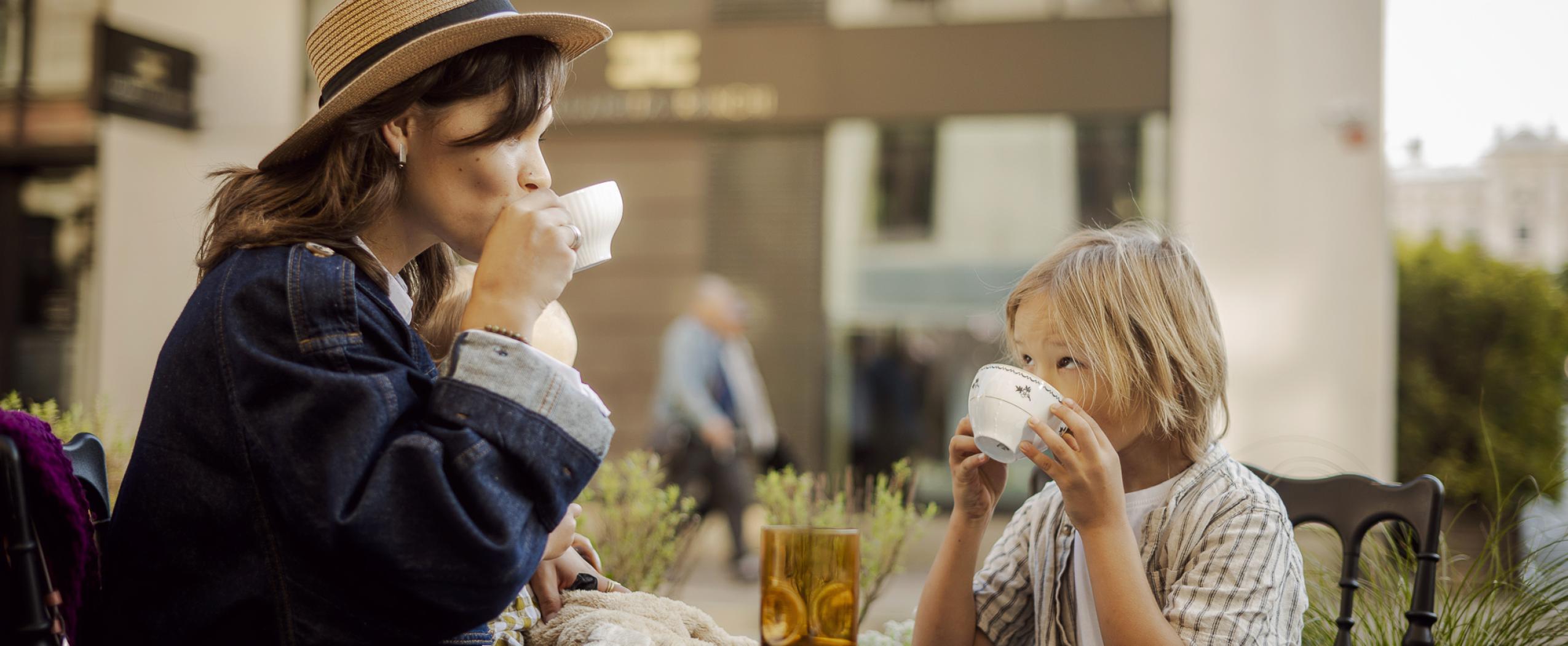 Jauna sieviete ar diviem maziem bērniem sēž kafejnīcā un izbauda laiku, fonā redzams CENTRUS kvartāls Dzirnavu ielā.
